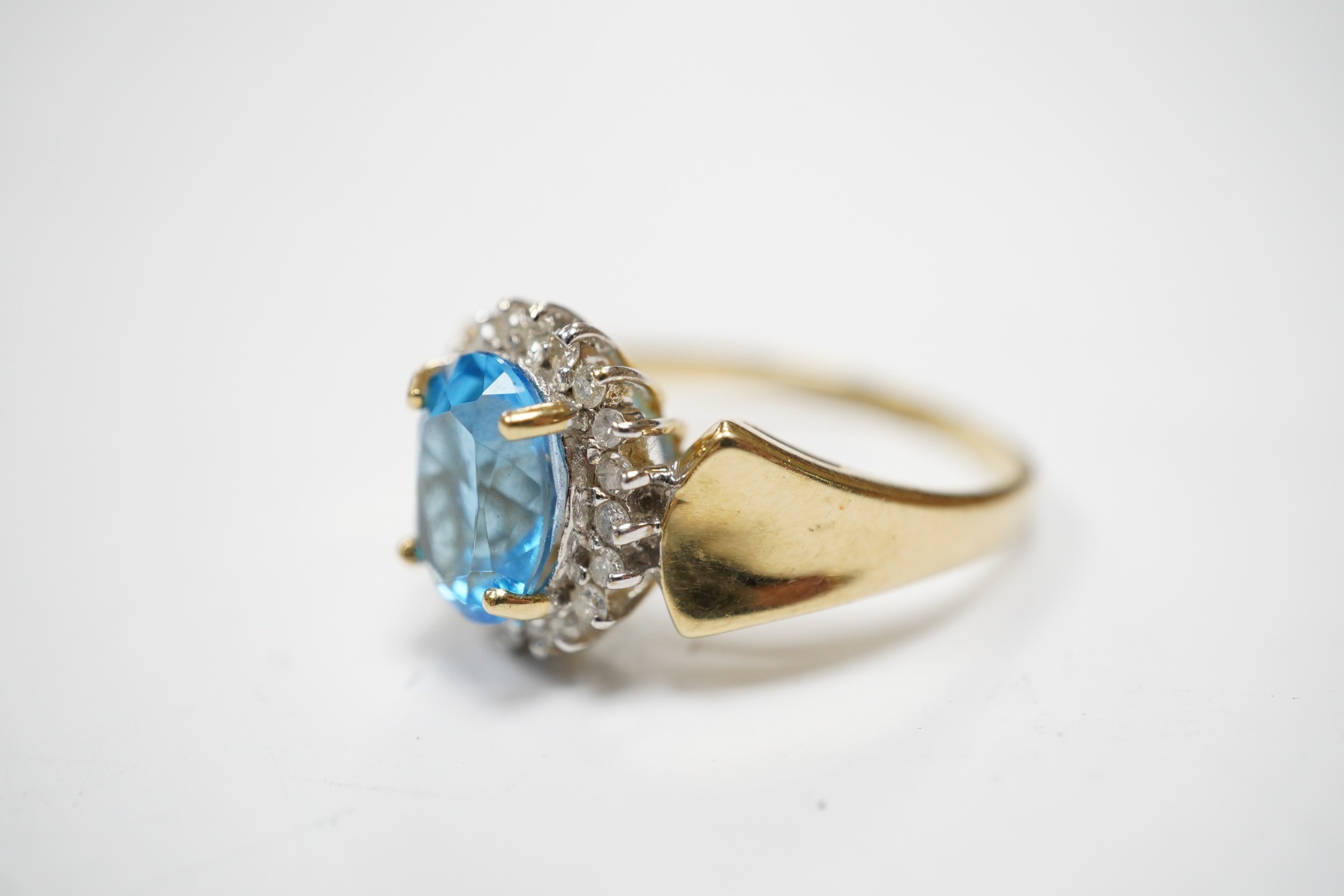 A modern 14k and oval cut blue topaz set dress ring, bordered with diamonds, size R, gross weight 4.7 grams. Condition - fair to good.